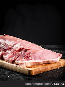 Raw pork sliced on a wooden cutting board. On a black background. High quality photo. Raw pork sliced on a wooden cutting board.