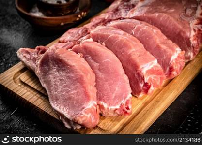 Raw pork sliced on a wooden cutting board. On a black background. High quality photo. Raw pork sliced on a wooden cutting board.