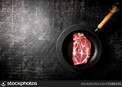 Raw pork steak in a frying pan. On a black background. High quality photo. Raw pork steak in a frying pan.