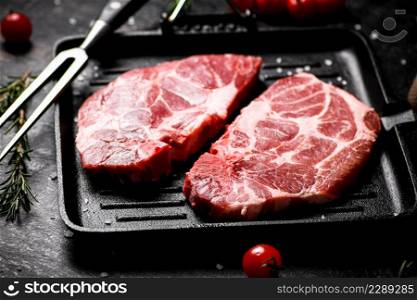 Raw pork steak in a frying pan with bay leaves and rosemary. Against a dark background. High quality photo. Raw pork steak in a frying pan with bay leaves and rosemary.