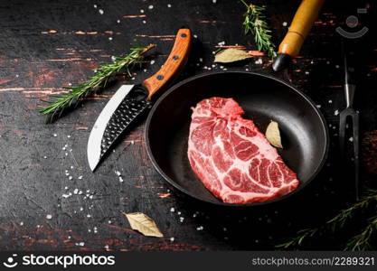 Raw pork steak in a frying pan with bay leaves and rosemary. Against a dark background. High quality photo. Raw pork steak in a frying pan with bay leaves and rosemary.