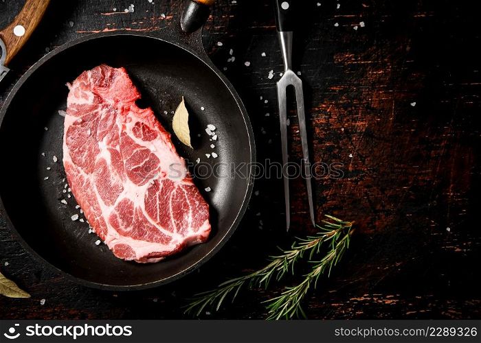 Raw pork steak in a frying pan with bay leaves and rosemary. Against a dark background. High quality photo. Raw pork steak in a frying pan with bay leaves and rosemary.