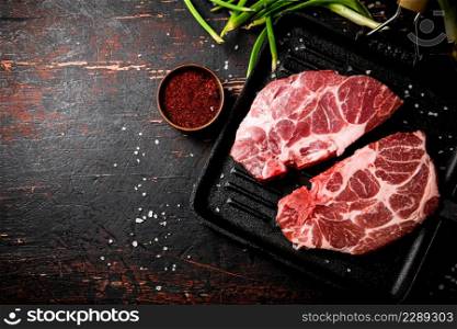 Raw pork steak in a frying pan with green onions and spices. Against a dark background. High quality photo. Raw pork steak in a frying pan with green onions and spices.