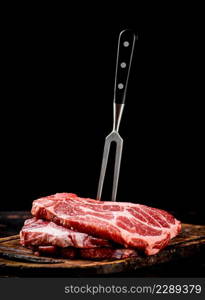 Raw pork steak on a cutting board with fork. On a black background. High quality photo. Raw pork steak on a cutting board with fork.