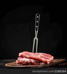 Raw pork steak on a cutting board with fork. On a black background. High quality photo. Raw pork steak on a cutting board with fork.