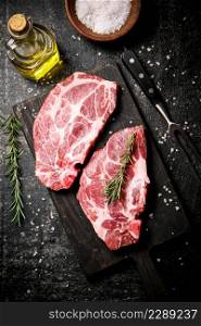 Raw pork steak on a cutting board with rosemary. On a black background. High quality photo. Raw pork steak on a cutting board with rosemary.