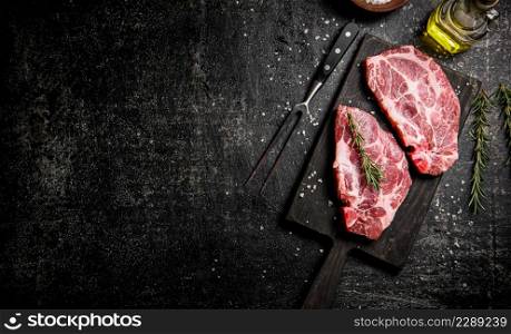 Raw pork steak on a cutting board with rosemary. On a black background. High quality photo. Raw pork steak on a cutting board with rosemary.
