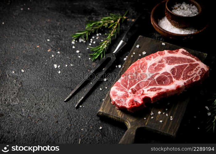 Raw pork steak on a cutting board with spices and rosemary. On a black background. High quality photo. Raw pork steak on a cutting board with spices and rosemary.