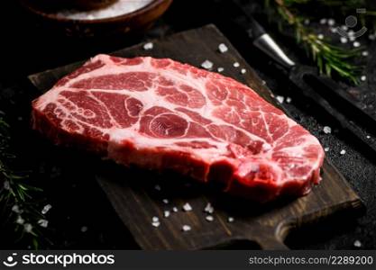 Raw pork steak on a cutting board with spices and rosemary. On a black background. High quality photo. Raw pork steak on a cutting board with spices and rosemary.