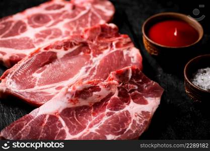 Raw pork steak on a stone board. On a black background. High quality photo. Raw pork steak on a stone board.
