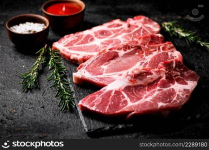 Raw pork steak on a stone board with tomato sauce, rosemary and spices. On a black background. High quality photo. Raw pork steak on a stone board with tomato sauce, rosemary and spices.