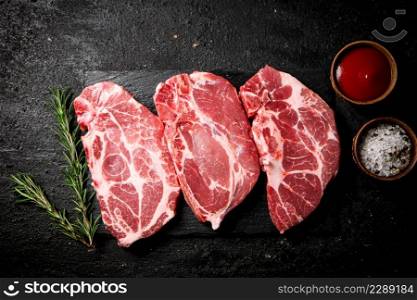 Raw pork steak on a stone board with tomato sauce, rosemary and spices. On a black background. High quality photo. Raw pork steak on a stone board with tomato sauce, rosemary and spices.