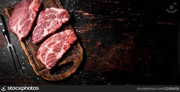 Raw pork steak on a wooden cutting board. Against a dark background. High quality photo. Raw pork steak on a wooden cutting board.