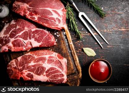 Raw pork steak on a wooden cutting board. Against a dark background. High quality photo. Raw pork steak on a wooden cutting board.