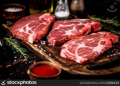 Raw pork steak on a wooden cutting board with tomato sauce and rosemary. Against a dark background. High quality photo. Raw pork steak on a wooden cutting board with tomato sauce and rosemary.
