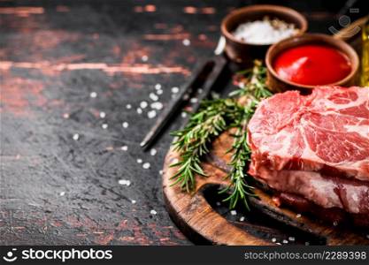 Raw pork steak on a wooden cutting board with tomato sauce, rosemary and spices. Against a dark background. . Raw pork steak on a wooden cutting board with tomato sauce,rosemary and spices.