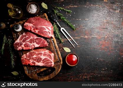 Raw pork steak on a wooden cutting board with tomato sauce, rosemary and spices. Against a dark background. . Raw pork steak on a wooden cutting board with tomato sauce,rosemary and spices.