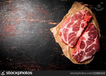 Raw pork steak on paper on the table. Against a dark background. High quality photo. Raw pork steak on paper on the table.