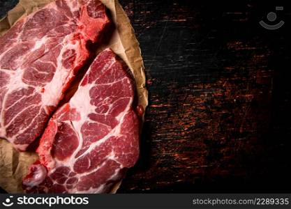 Raw pork steak on paper on the table. Against a dark background. High quality photo. Raw pork steak on paper on the table.