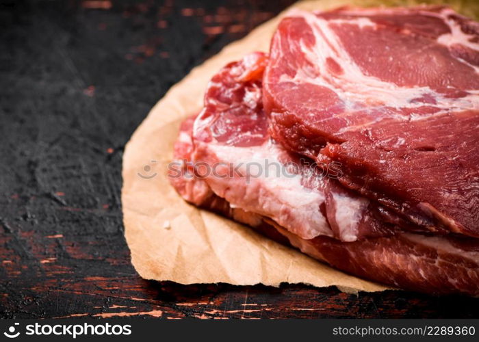 Raw pork steak on paper on the table. Against a dark background. High quality photo. Raw pork steak on paper on the table.