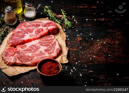 Raw pork steak on paper with rosemary. Against a dark background. High quality photo. Raw pork steak on paper with rosemary.