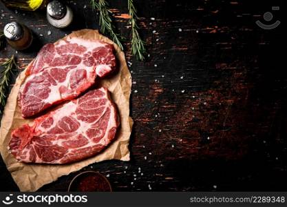 Raw pork steak on paper with rosemary. Against a dark background. High quality photo. Raw pork steak on paper with rosemary.