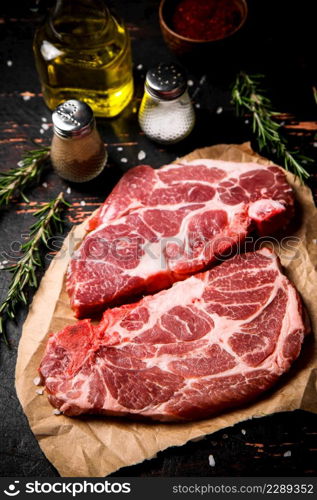 Raw pork steak on paper with rosemary. Against a dark background. High quality photo. Raw pork steak on paper with rosemary.