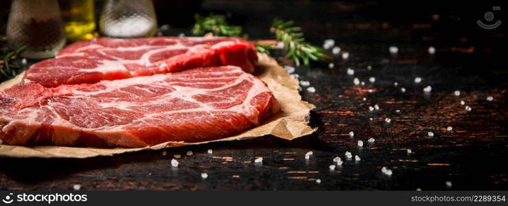 Raw pork steak on paper with rosemary. Against a dark background. High quality photo. Raw pork steak on paper with rosemary.