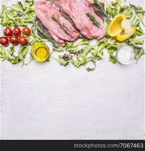 raw pork steak on vintage cutting board with lettuce, cherry tomatoes, bell pepper, oil and spices on wooden rustic background top view close up