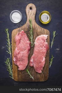 raw pork steak on vintage cutting board with rosemary, oil and salt on wooden rustic background top view close up
