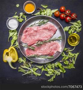 raw pork steak on vintage frying pan with salad, cherry tomatoes, bell pepper, oil and spices on wooden rustic background top view close up