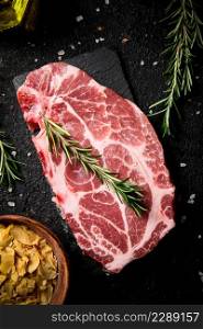 Raw pork steak with a sprig of rosemary on a stone board. On a black background. High quality photo. Raw pork steak with a sprig of rosemary on a stone board.