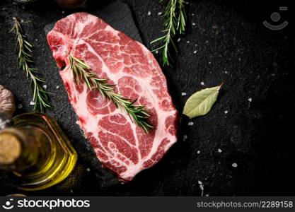 Raw pork steak with a sprig of rosemary on a stone board. On a black background. High quality photo. Raw pork steak with a sprig of rosemary on a stone board.