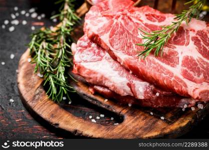 Raw pork steak with rosemary. Against a dark background. High quality photo. Raw pork steak with rosemary.