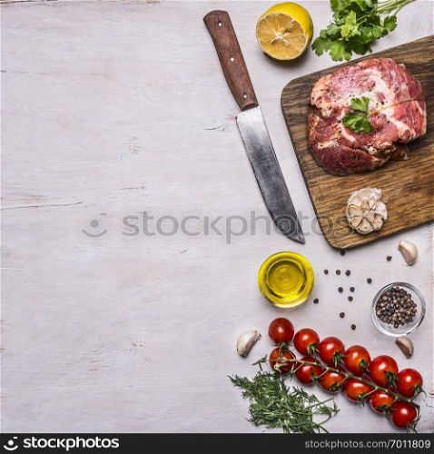 raw pork steak with spices, garlic and herbs, lemon and butter knife for meat, tomatoes on a branch, black pepper, dill, border, with text area on wooden rustic background top view