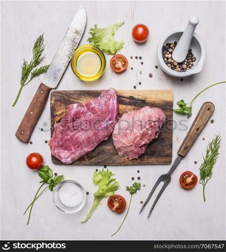 raw Pork steak with vegetables and herbs, meat knife and fork, on a cutting board on wooden rustic background top view close up