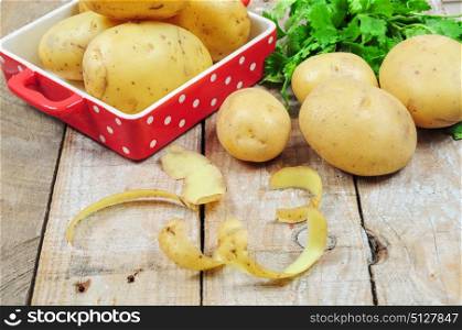 Raw potatoes and potato peels on wooden table, tray of more potatoes on the background