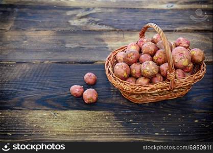 Raw potatoes in a wicker basket on a brown wood background, top view