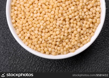 Raw ptitim pasta in a ceramic bowl on a dark concrete background. Israeli food preparation