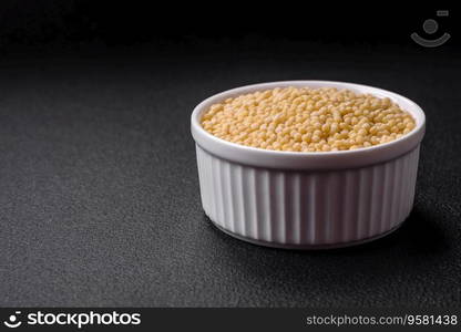 Raw ptitim pasta in a ceramic bowl on a dark concrete background. Israeli food preparation