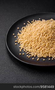 Raw ptitim pasta in a ceramic bowl on a dark concrete background. Israeli food preparation