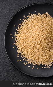 Raw ptitim pasta in a ceramic bowl on a dark concrete background. Israeli food preparation