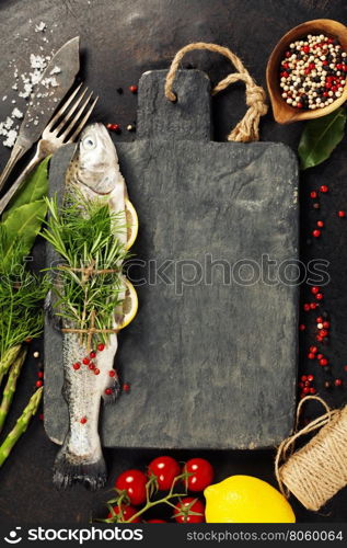 Raw rainbow trout with lemon, herbs and spice on rustic background