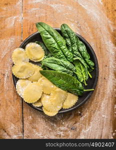 raw ravioli with fresh spinach leaves in gray plate on wooden background with meal, top view