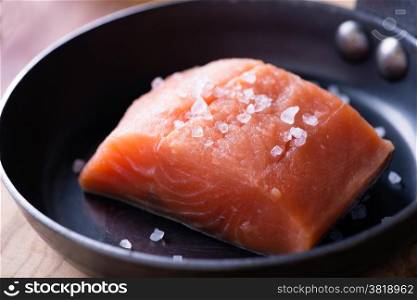 Raw red fish fillet with sea salt on frying pan, close up, selective focus
