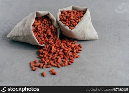 Raw red organic goji berries in small rustic sacks and spread on grey background. Food and nutrition concept. Wolfberries for eating