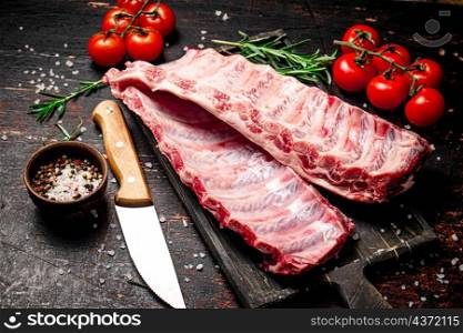 Raw ribs on a cutting board with a knife and tomatoes. Against a dark background. High quality photo. Raw ribs on a cutting board with a knife and tomatoes.