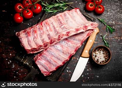 Raw ribs on a cutting board with a knife and tomatoes. Against a dark background. High quality photo. Raw ribs on a cutting board with a knife and tomatoes.