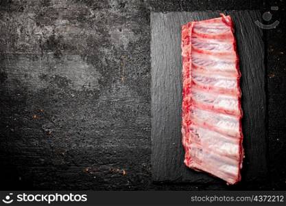 Raw ribs on a stone board. On a black background. High quality photo. Raw ribs on a stone board.