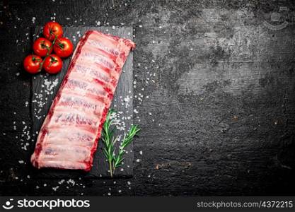 Raw ribs on a stone board with tomatoes and pieces of salt. On a black background. High quality photo. Raw ribs on a stone board with tomatoes and pieces of salt.
